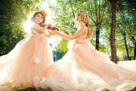 Classical music. Beautiful fairy girl teaches to play the violin a little girl. Musical fairy tales.の写真素材