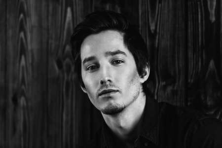 Vogue shot of a handsome male model in a denim shirt standing by a wooden wall. Men's beauty, fashion. の写真素材