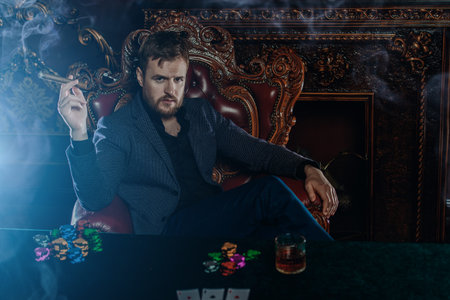 A wealthy mature man smoking cigar and playing poker in a casino. Gambling, playing cards and...