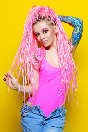 Stylish girl with pink dreadlocks posing in bright clothes on a yellow background. Beauty, fashion.