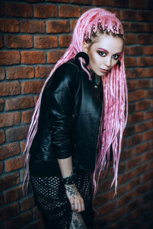 Sexy hipster girl with pink dreadlocks posing by the brick wall. Beauty, fashion.の写真素材