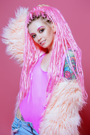 Stylish girl with pink dreadlocks posing in bright clothes on a pink background. Beauty, fashion.の写真素材