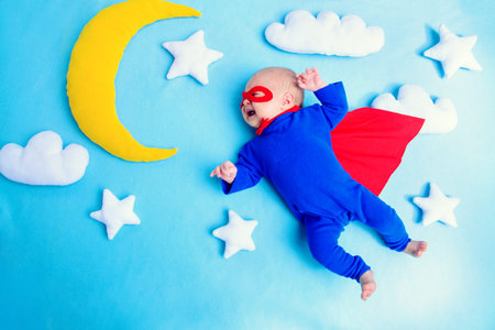 Little baby superhero with red cape flies through the night sky.