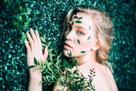 Beautiful young woman with green leaves on her face over green background. Cosmetics and makeup.の写真素材