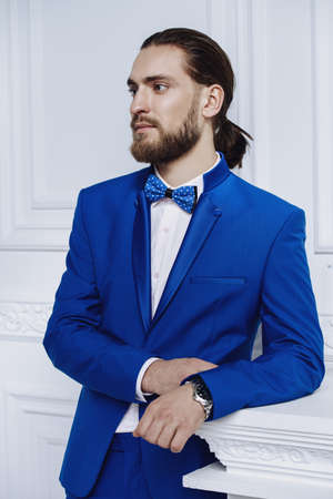 Fashion shot. Handsome young man posing in elegant blue suit in luxurious apartments. Hair styling, barbershop. Men's beauty, fashion.の写真素材