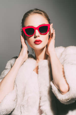 Gorgeous blonde woman posing in luxurious fur coat and pin-up sunglasses. Fashion, beauty. Studio shot.の写真素材