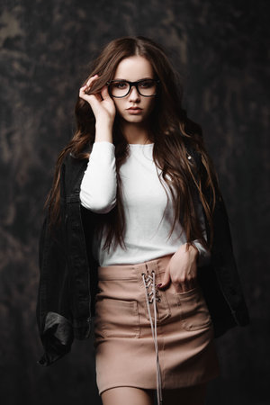Portrait of a attractive young woman in modern youth clothes and glasses. Studio shot over dark...