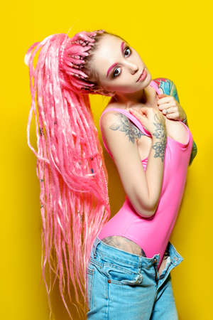 Stylish girl with pink dreadlocks posing in bright clothes on a yellow background. Beauty, fashion.の写真素材