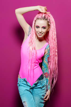 Stylish girl with pink dreadlocks posing in bright clothes on a pink background. Beauty, fashion.の写真素材