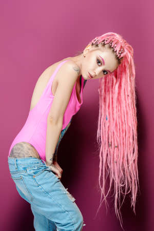 Stylish girl with pink dreadlocks posing in bright clothes on a pink background. Beauty, fashion.の写真素材