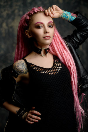 Stunning female model with pink dreadlocks posing on a dark background. Trendy hairstyles. Beauty,...