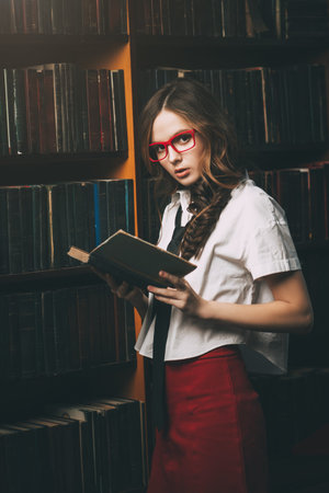 Beautiful girl wearing school uniform stands in the old library. Beauty, fashion. Educational...