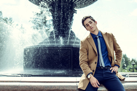 Happy young man in elegant clothes walking in a city park. Outdoor fashion. Business style. の写真素材