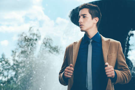 Happy young man in elegant clothes walking in a city park. Outdoor fashion. Business style. の写真素材
