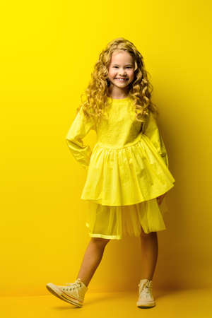 Children's fashion. Beautiful  little girl in yellow dress posing at studio over yellow background.の写真素材