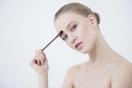 Close-up portrait of a beautiful young woman applying makeup brush. Beauty, cosmetics makeup.の写真素材