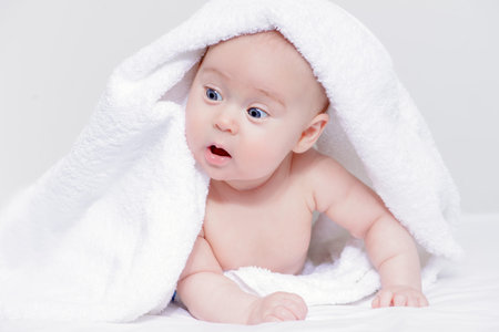 Sweet baby under a white towel after bath. Healthcare, pediatrics.