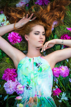 Beauty portrait. Gorgeous young woman with beautiful long hair lying on a grass among fresh summer flowers. Perfume, cosmetics. Fashion concept. の写真素材