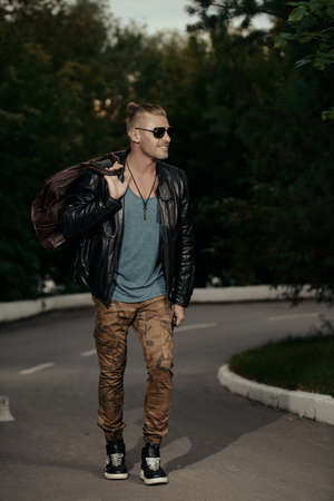 Handsome brutal man in leather jacket walking down the road. Biker man is going to trip. The spirit of independence.の写真素材