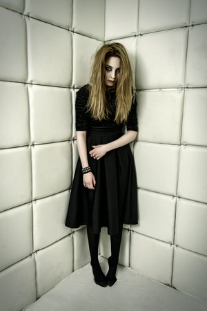 Portrait of a beautiful crazy girl dressed in black gothic dress in an isolated room in a madhouse.
