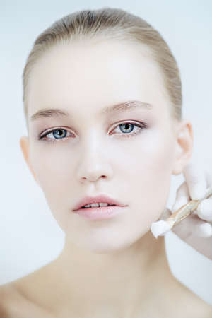 Close-up portrait of a beautiful young woman applying makeup brush. Beauty, cosmetics makeup.の写真素材