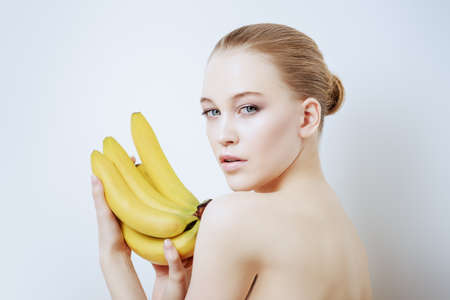 Beauty, natural cosmetics concept. Beautiful young woman with healthy shiny skin holding bananas. White background. の写真素材