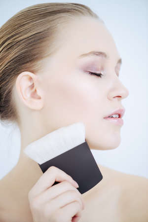 Close-up portrait of a beautiful young woman applying makeup brush. Beauty, cosmetics makeup.の写真素材