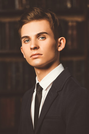Intelligent student boy in elegant clothes standing in the library. Fashion. Educational concept.