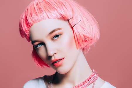 Close-up portrait of a cheerful girl with bright pink hair wearing white T-shirt over pink background.  Beauty, fashion concept.の写真素材