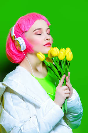 Trendy vivid girl with pink hair wearing headphones holding flowers. Green background. Beauty, fashion, youth style.の写真素材