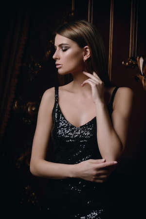 Portrait of an attractive young woman in tight black dress in a luxury apartment. Classic vintage interior. Beauty, fashion.の写真素材