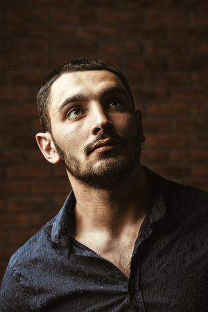 Portrait of a handsome brunet man standing by a brick wall. Men's beauty, fashion. Men's barbershop,...