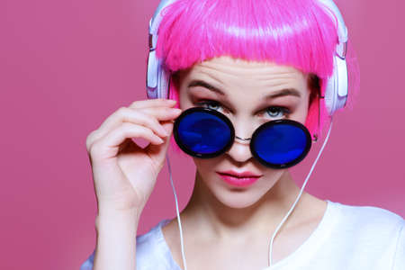 Trendy girl with pink hair wearing sunglasses enjoys the music on headphones. Pink background. Youth style, leisure.の写真素材