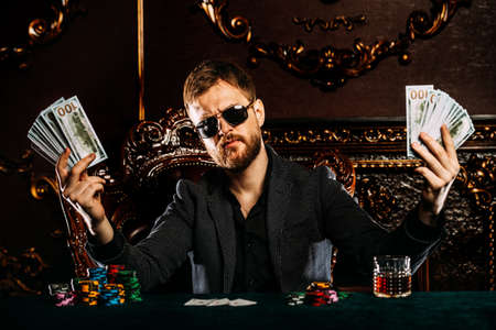 A wealthy mature man smoking cigar and playing poker in a casino. Gambling, playing cards and roulette.の写真素材
