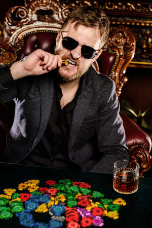 A wealthy mature man smoking cigar and playing poker in a casino. Gambling, playing cards and roulette.の写真素材