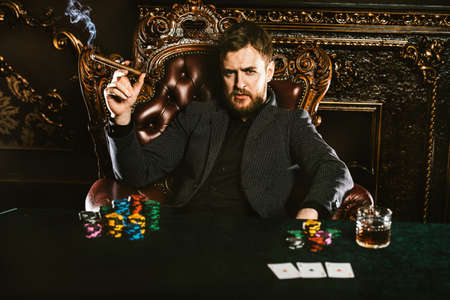 A wealthy mature man smoking cigar and playing poker in a casino. Gambling, playing cards and roulette.の写真素材