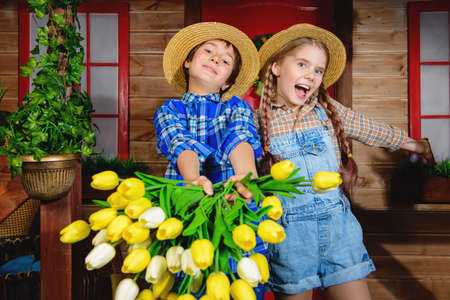 Happy children are posing on the porch of a village house with a bouquet of spring flowers. Happy childhood. Spring holidays.の写真素材