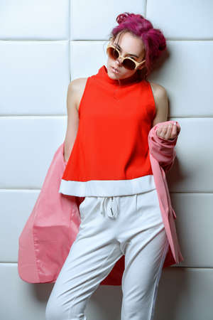 Pretty pink-haired girl in bright summer clothes and sunglasses posing on a light background. Fashion, beauty. Optics style. Youth style.の写真素材