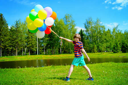 Happy boy enjoys with a sunny summer day and balloons. Summer holidays. Birthday.の写真素材