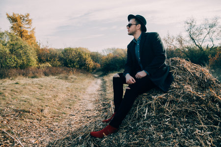 Autumn fashion. Handsome male model in black coat, a hat and sunglasses posing outdoor. Autumn...
