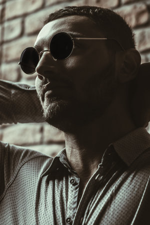 Close-up portrait of a handsome brunet man in sunglasses over brick wall background. Men's beauty,...