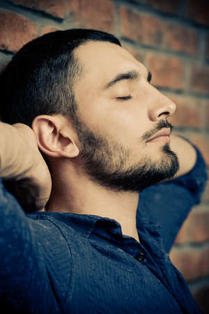 Close-up portrait of a handsome brunet man over brick wall background. Men's beauty, fashion. Men's barbershop, Hairstyle.の写真素材
