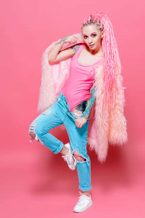 Stylish girl with pink dreadlocks posing in bright clothes on a pink background. Full length portrait. Beauty, fashion.の写真素材