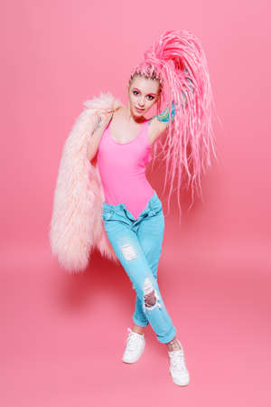 Stylish girl with pink dreadlocks posing in bright clothes on a pink background. Full length portrait. Beauty, fashion.の写真素材