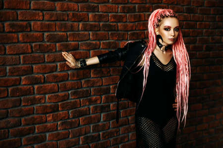 Sexy hipster girl with pink dreadlocks posing by the brick wall. Beauty, fashion.の写真素材