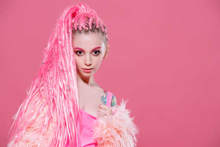 Stylish girl with pink dreadlocks posing in bright clothes on a pink background. Beauty, fashion.の写真素材