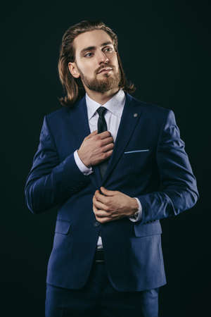 Fashion shot. Handsome young man posing in elegant suit and white shirt over black background. Men's beauty, fashion.の写真素材