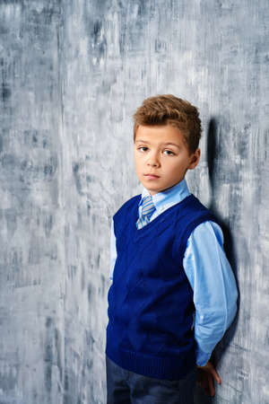 Portrait of a sad boy. Seven year old boy in elegant school clothes standing by a grey wall with a sad face. Loneliness.の写真素材