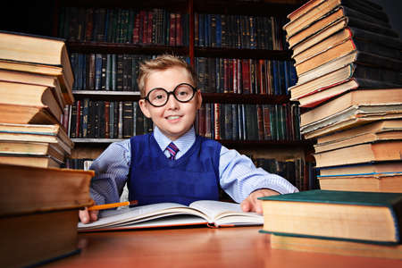 Smart boy in a suit sitting in the library by the bookshelves with many old books. Educational concept. Science.の写真素材