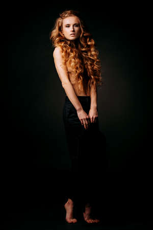 Portrait of a topless girl with long curly hair on a black background. Beauty, fashion.の写真素材